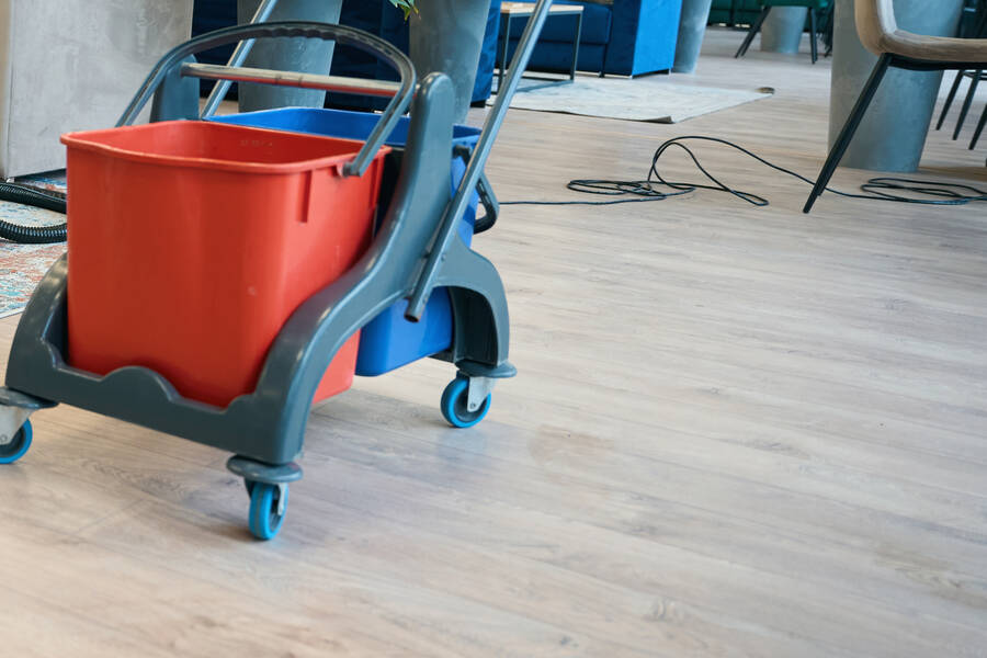A mop bucket and trolley on a wooden floor in a communal lounge